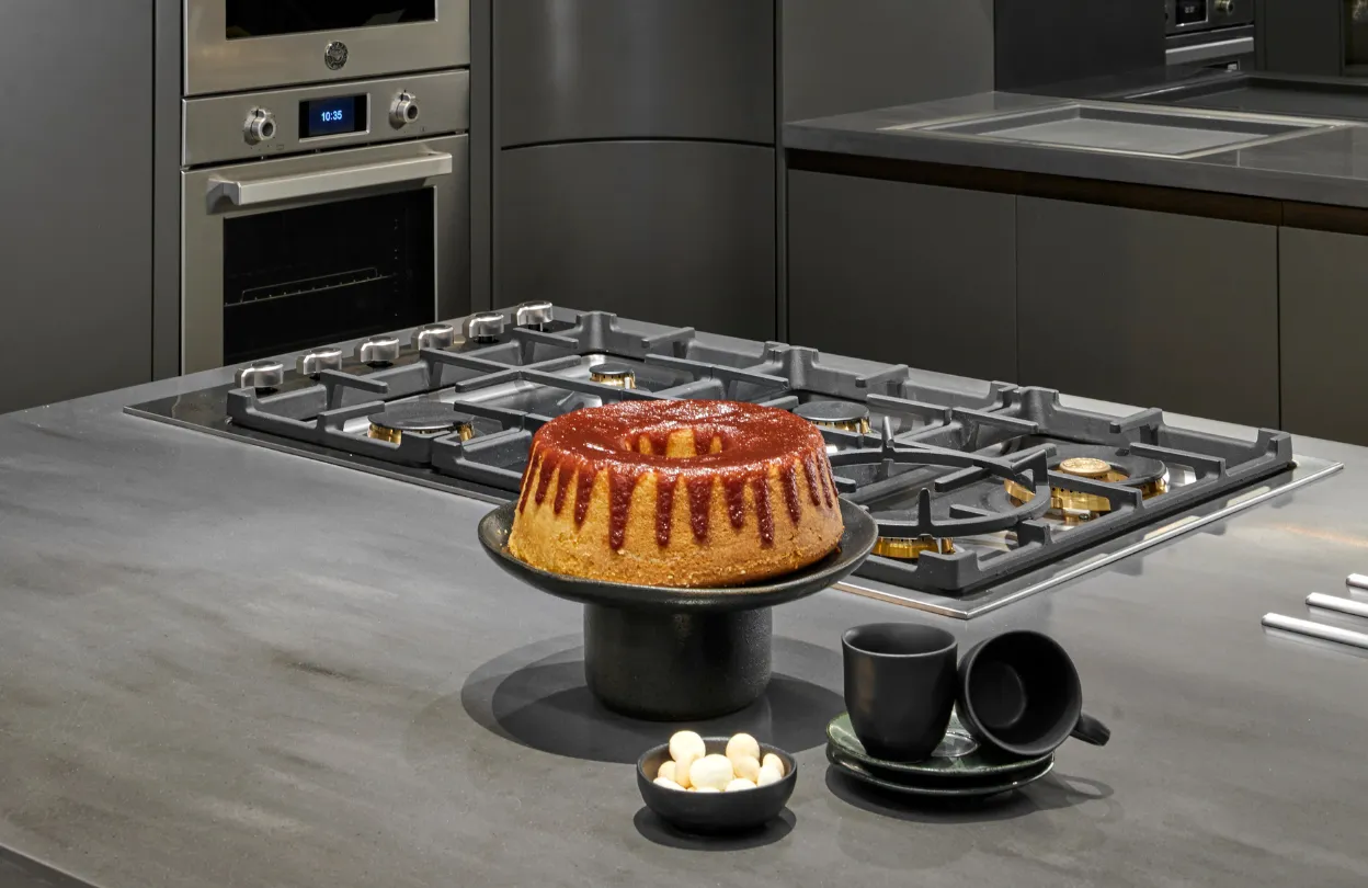Cooktop a gás com trempes de ferro em bancada cinza e forno embutido ao fundo